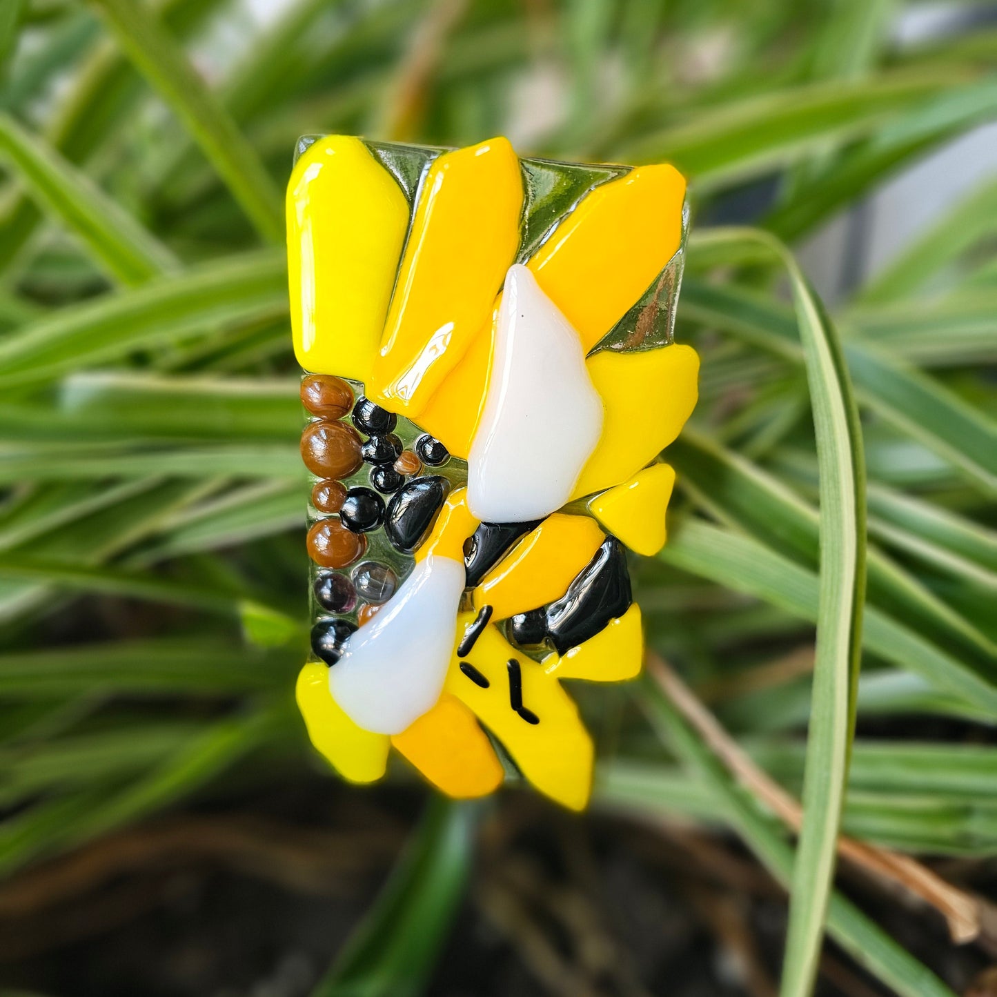 A fused glass garden stake that has an image of a sunflower with a bumble bee on it.