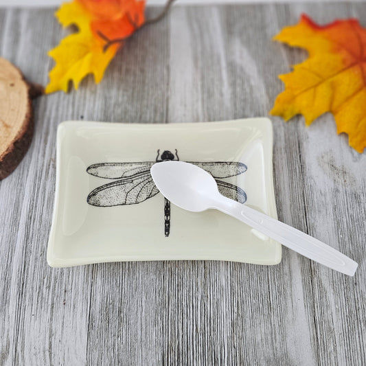A 4x6 dish, cream colored with a black outline of a dragonfly fused into the glass to be one solid piece. Used as a spoon rest.