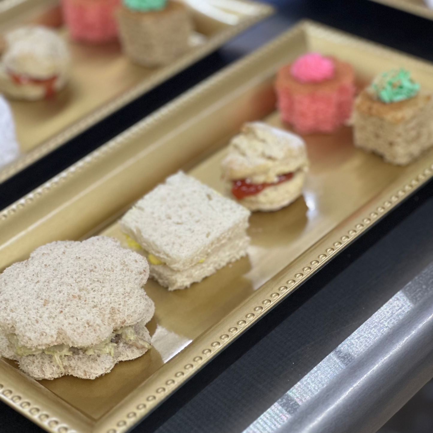 Small sandwiches and deserts on a decorative tray with a blurred background