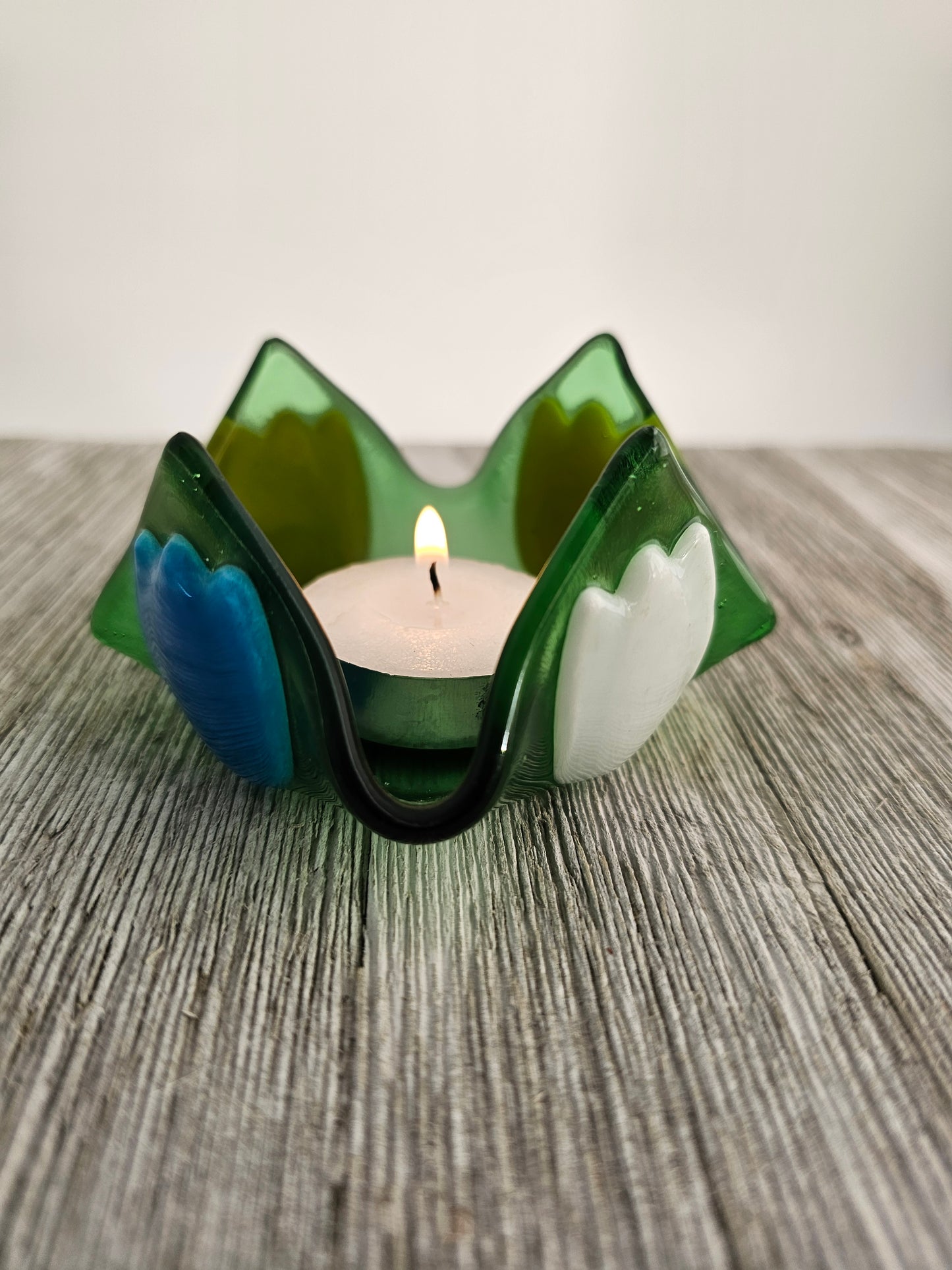 A green glass dish that comes to 4 points and has tulip of different color on each side.