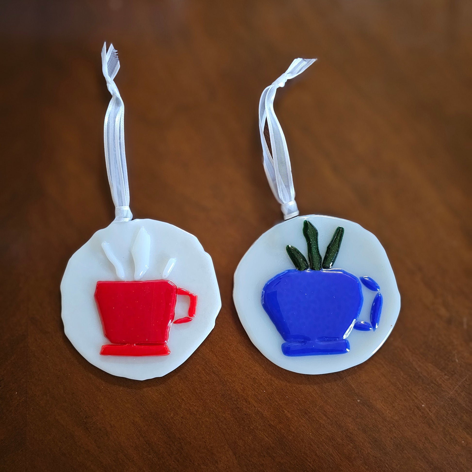 Two ornaments with teacups. A red teacup hints at the hot tea inside with white glass as steam. The blue cup has a succulent making it a little teacup plant pot image.