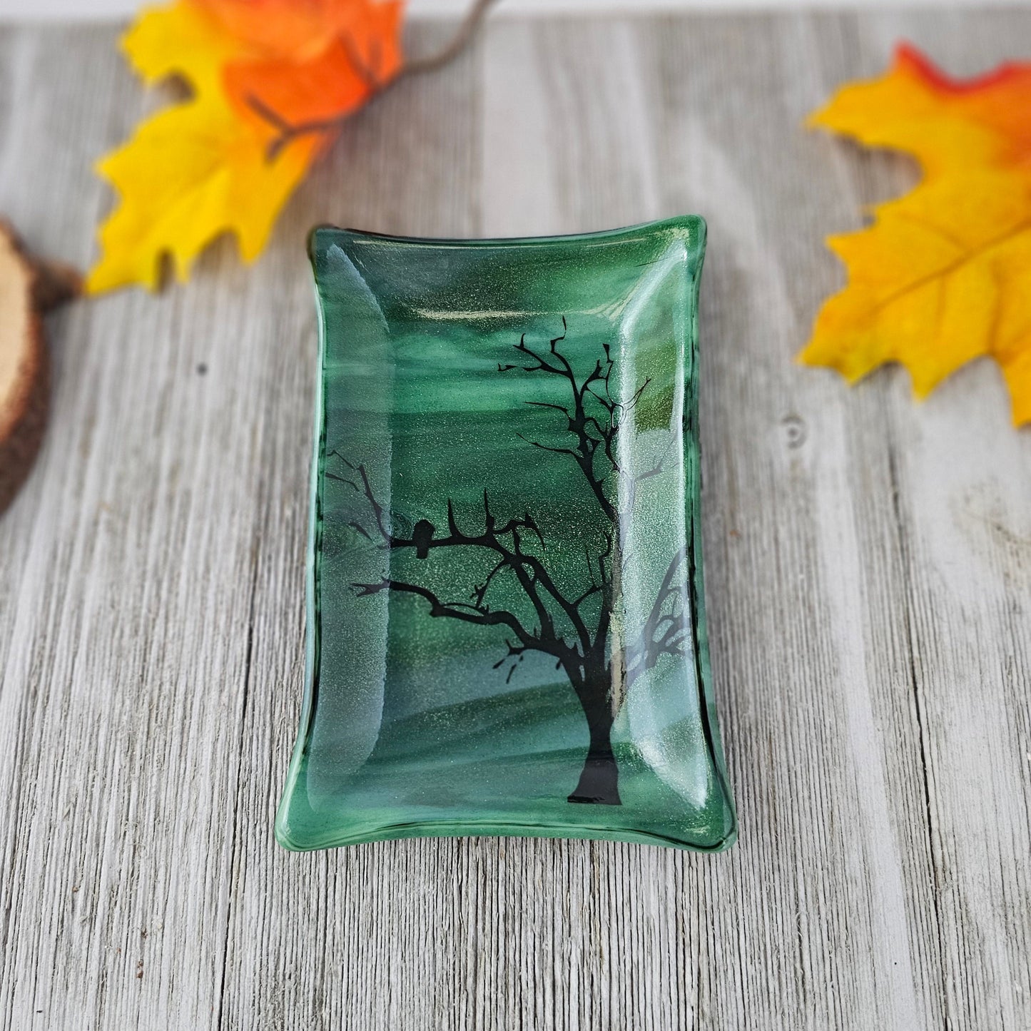 Fused glass with varied shades of green and a tree and bird design fused into the glass.