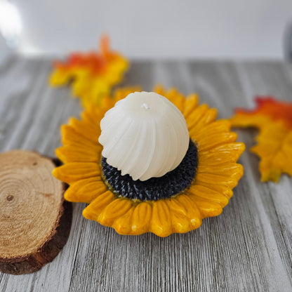 shades of yellow and orange sunflower with a dark brown center sitting on books holding a pillar candle.