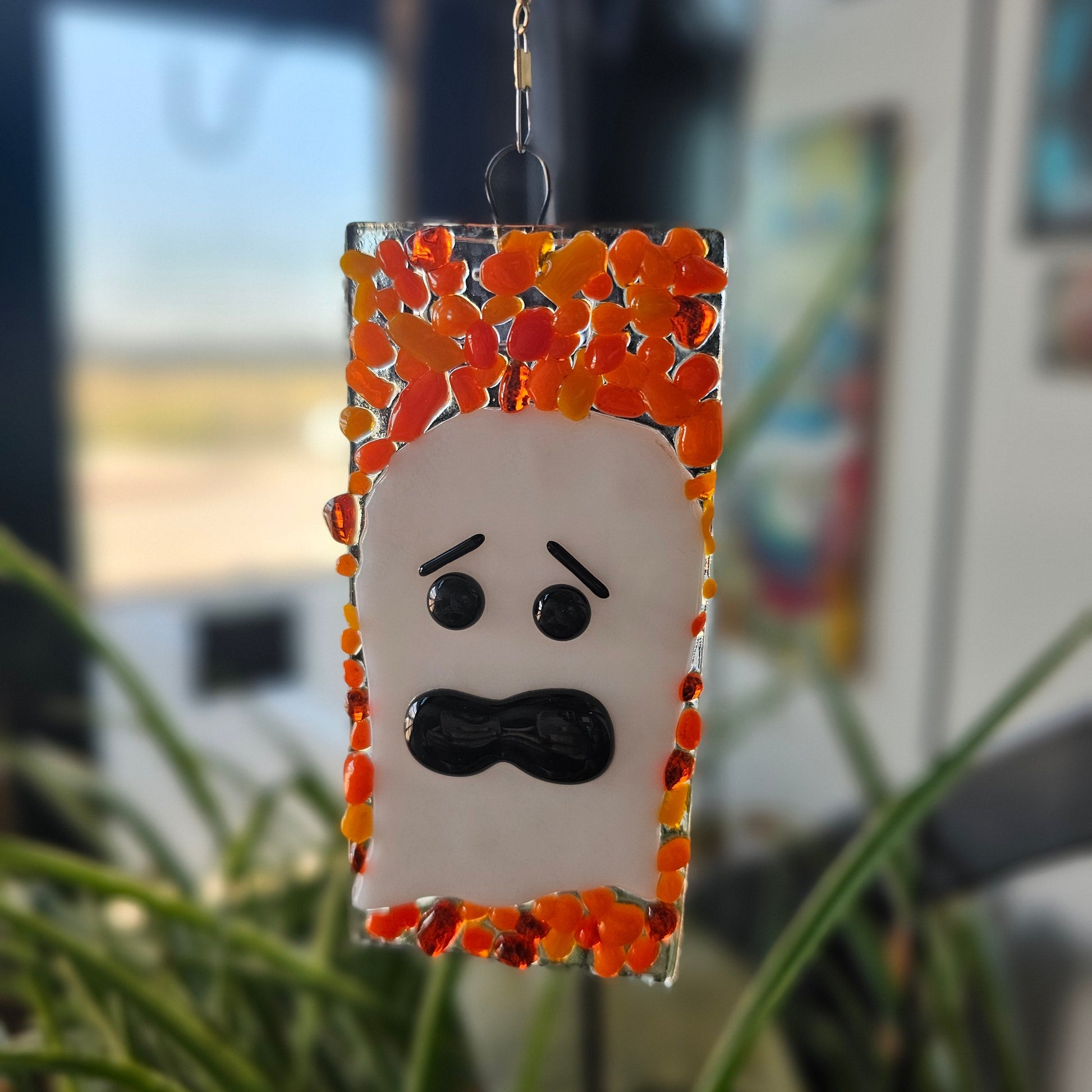 Ghost face design on a rectangular background with orange and black accents, blurred indoor background