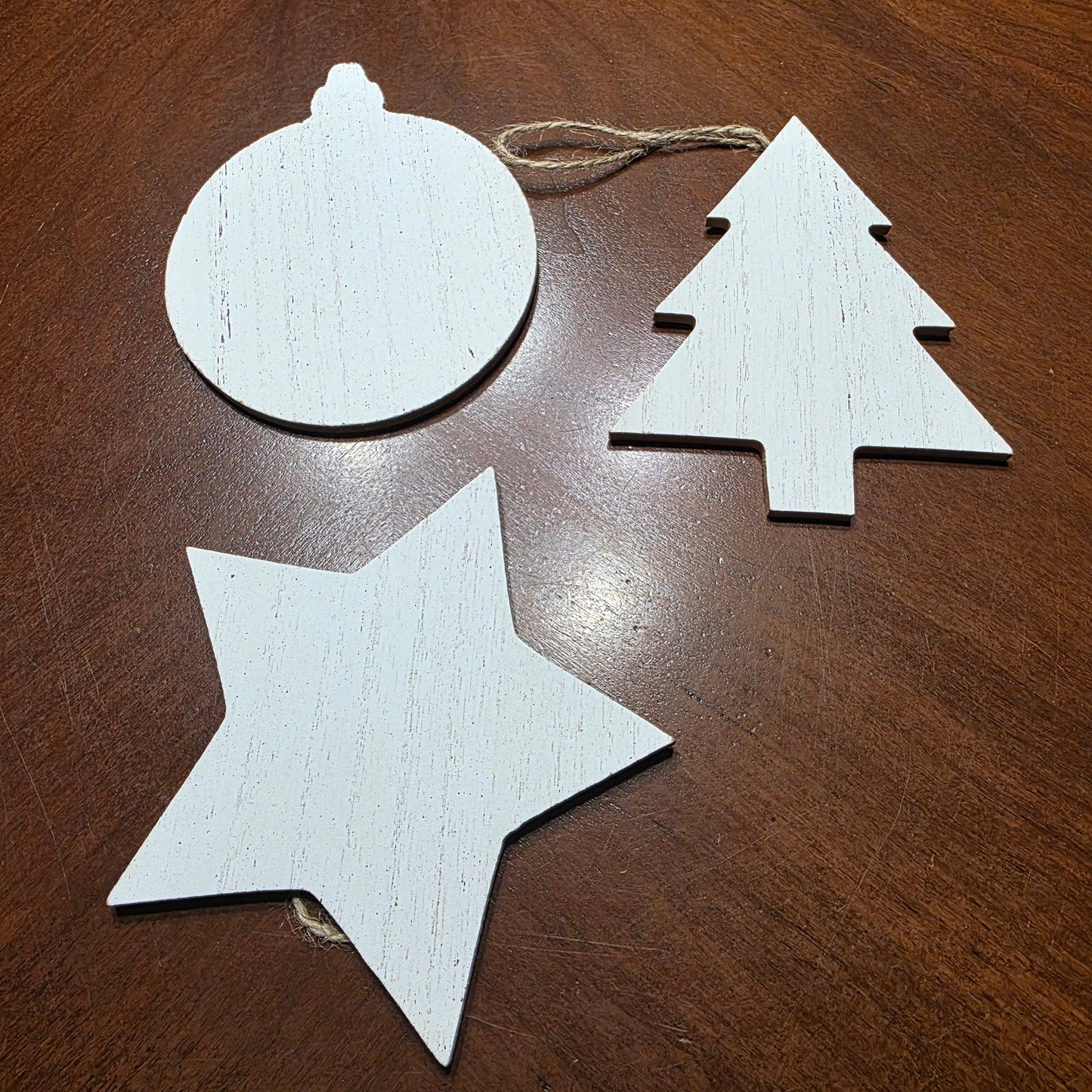 Three wooden Christmas ornaments shaped like a star, circle, and tree on a wooden surface.
