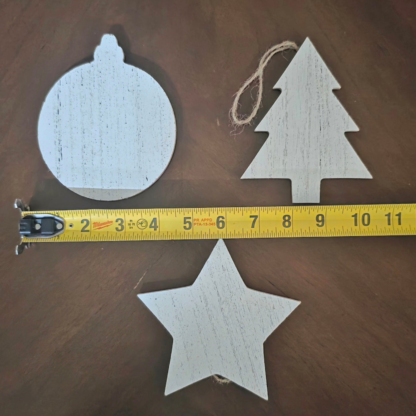 Wooden Christmas ornaments (sphere, tree, star) with a measuring tape on a wooden surface.  4" larger ornaments.