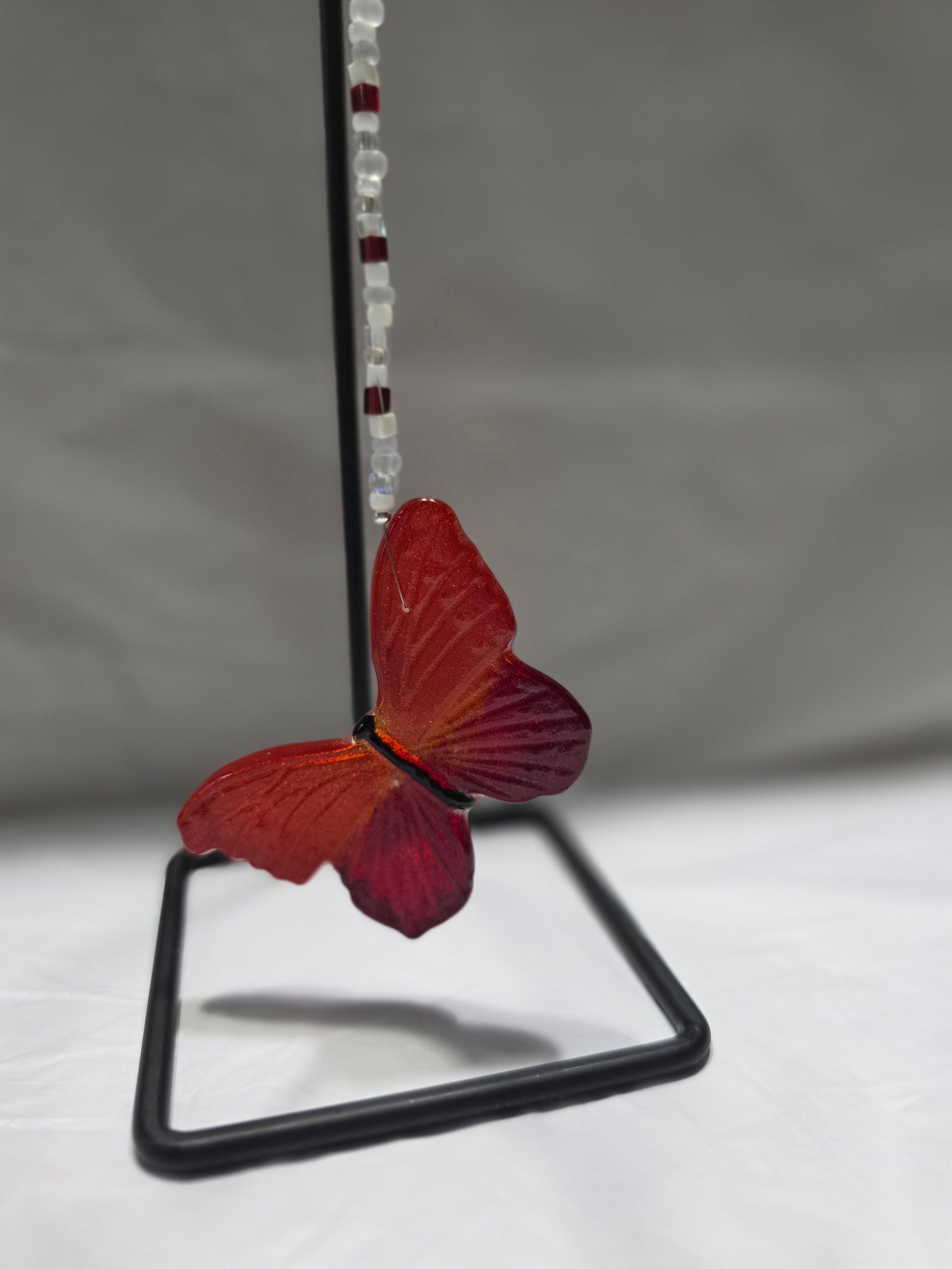 Red and orange butterfly hanging from a beaded wire against a white and gray background