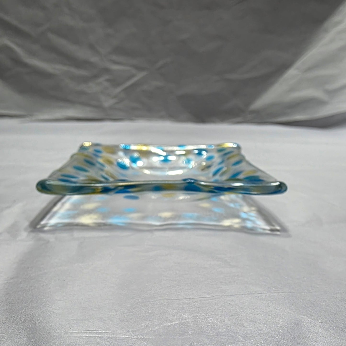 A clear dish with blues and yellow polka dots, sitting on a white surface. The colored dots reflect on the white surface from the rooms light source.