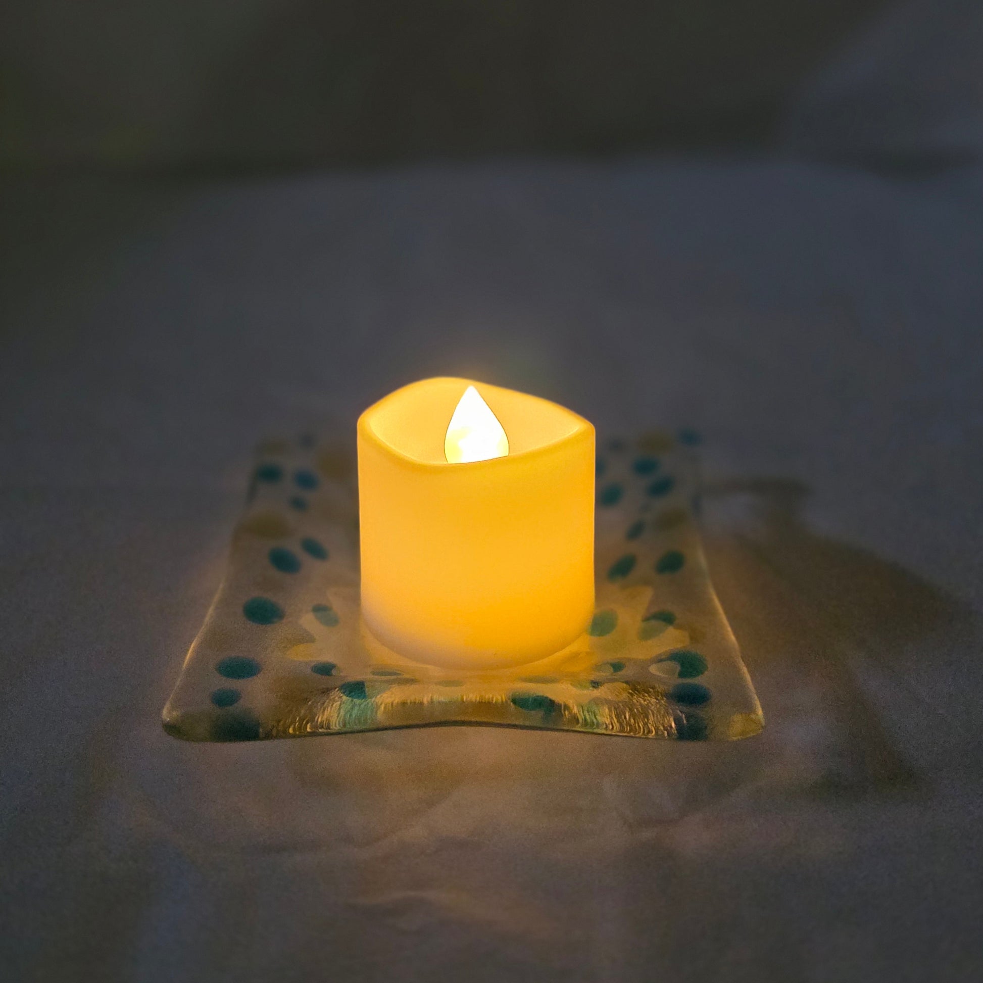 Small lit candle inside a decorative polka dot container on a white surface.