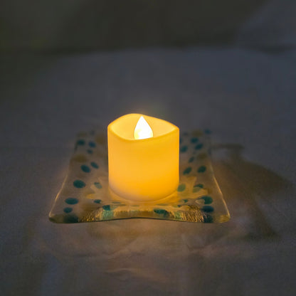 Small lit candle inside a decorative polka dot container on a white surface.
