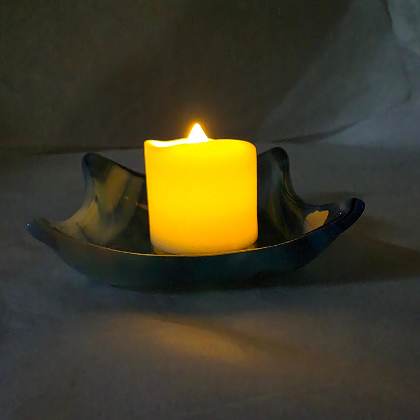 Various blue and white streaky, little dishes on a white surface, with a candle. Implying dish can be used as a candle holder.