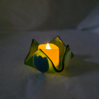 Small candle in a decorative green holder on a white surface