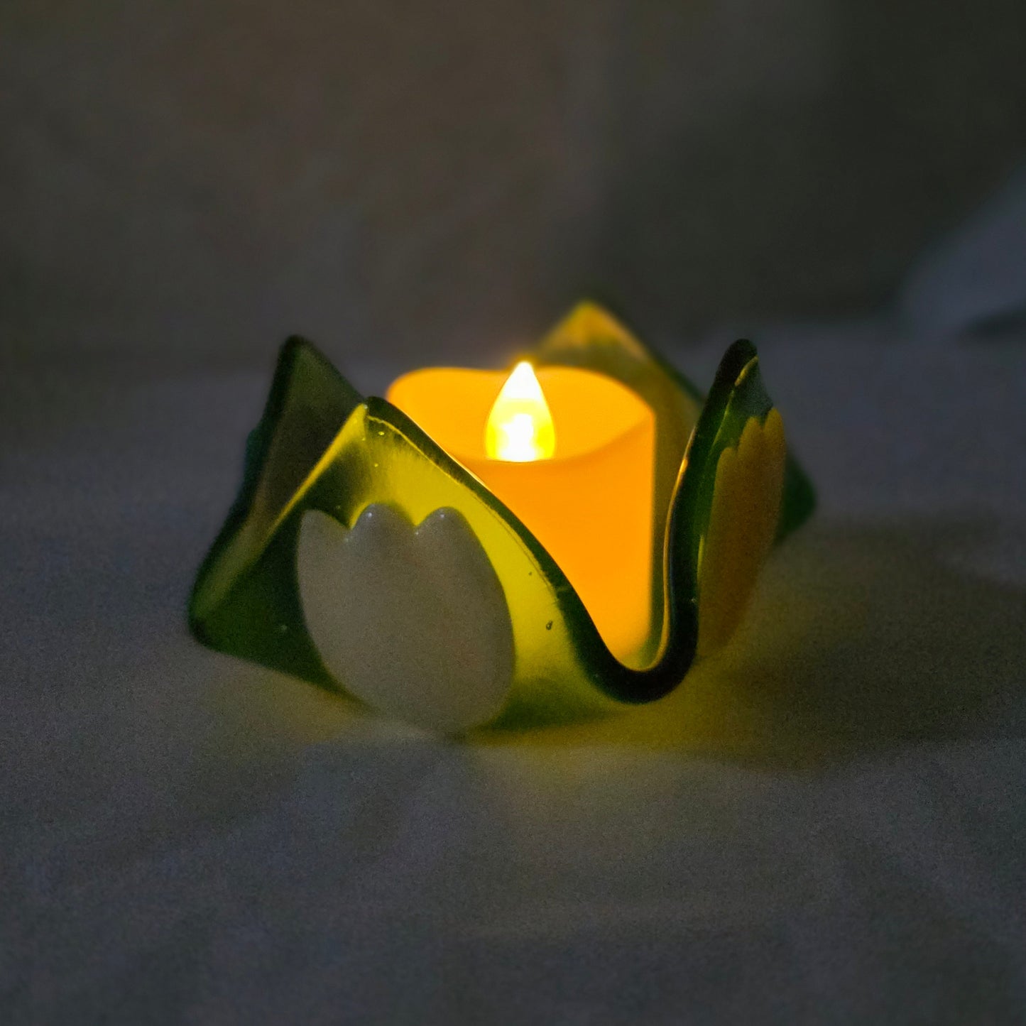 Green glass candle holder with a lit candle on a white background