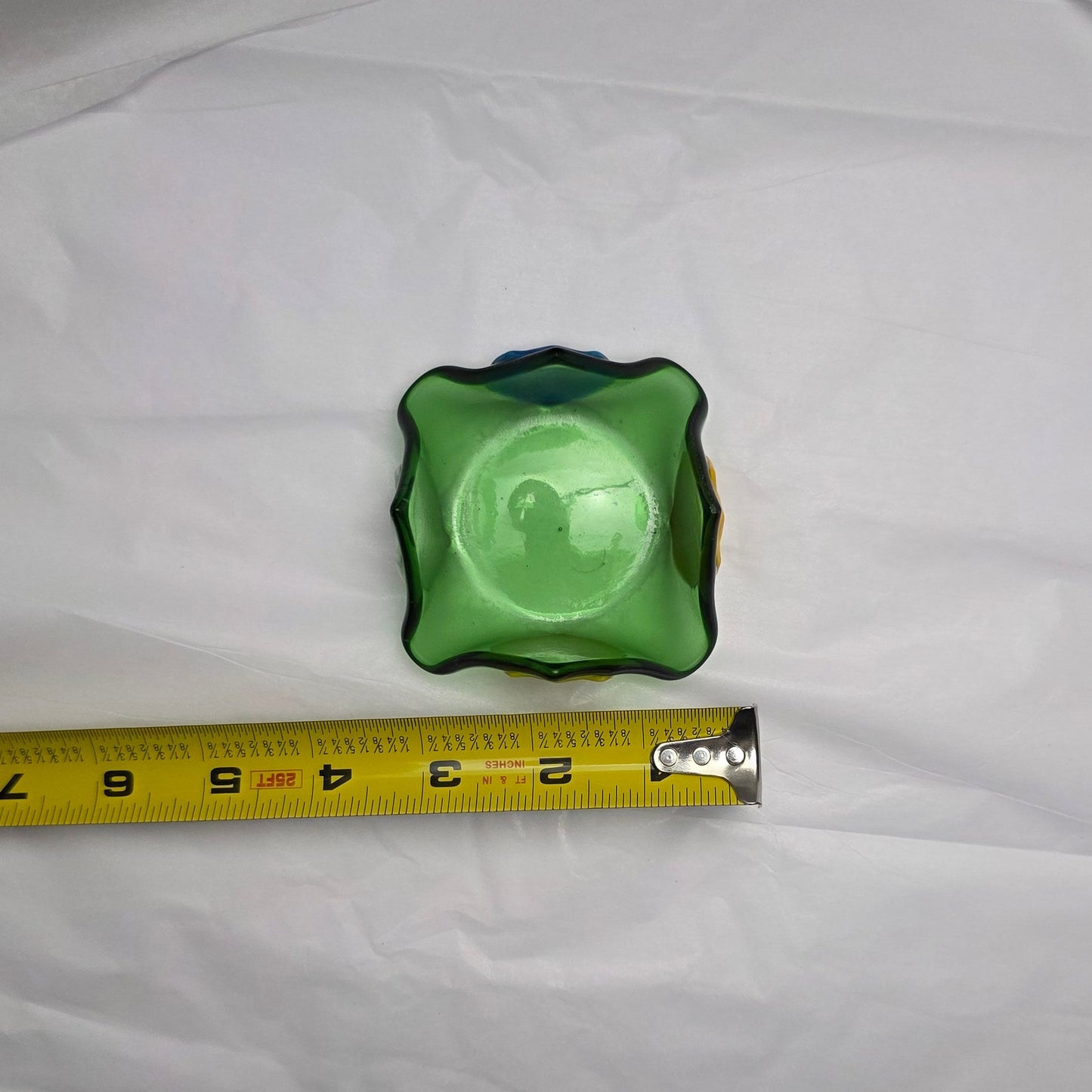 A green glass dish that comes to 4 points and has tulip of different color on each side. The holder is laying against a tape measure to show the approximate size: 3 inches.