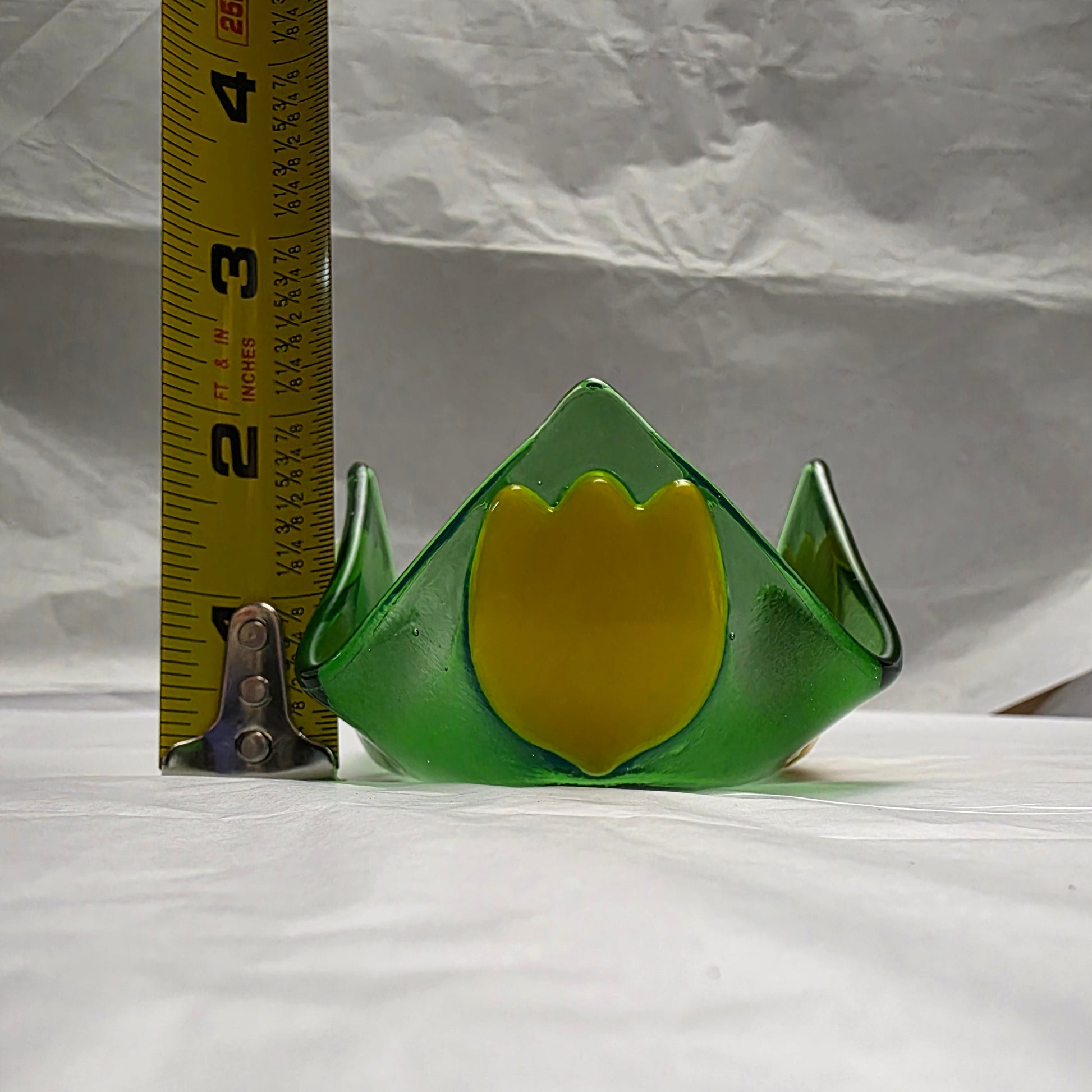 
A green glass dish that comes to 4 points and has tulip of different color on each side. The holder is laying against a tape measure to show approximate height: 2 inches.
