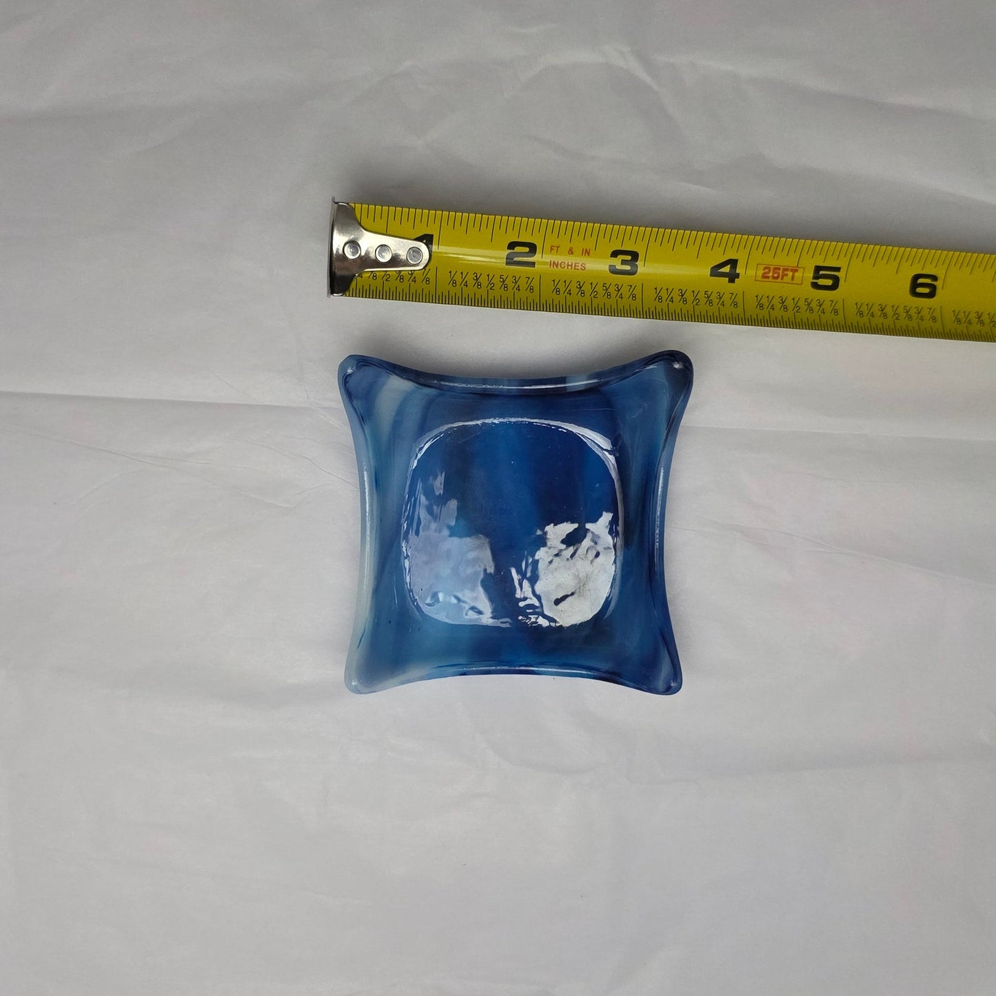 Blue and white streaky little dish, lying next to a tape measure on a white surface.  Approximately 3.5 in.