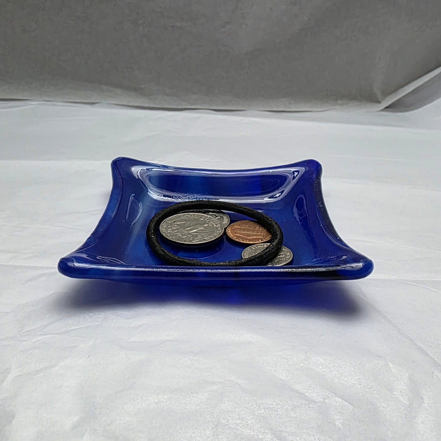 Various blue and white streaky colored little dish.  Dish is on a white surface. The little dish has coins and a hair tie indicating can be used as a trinket or ring dish.
