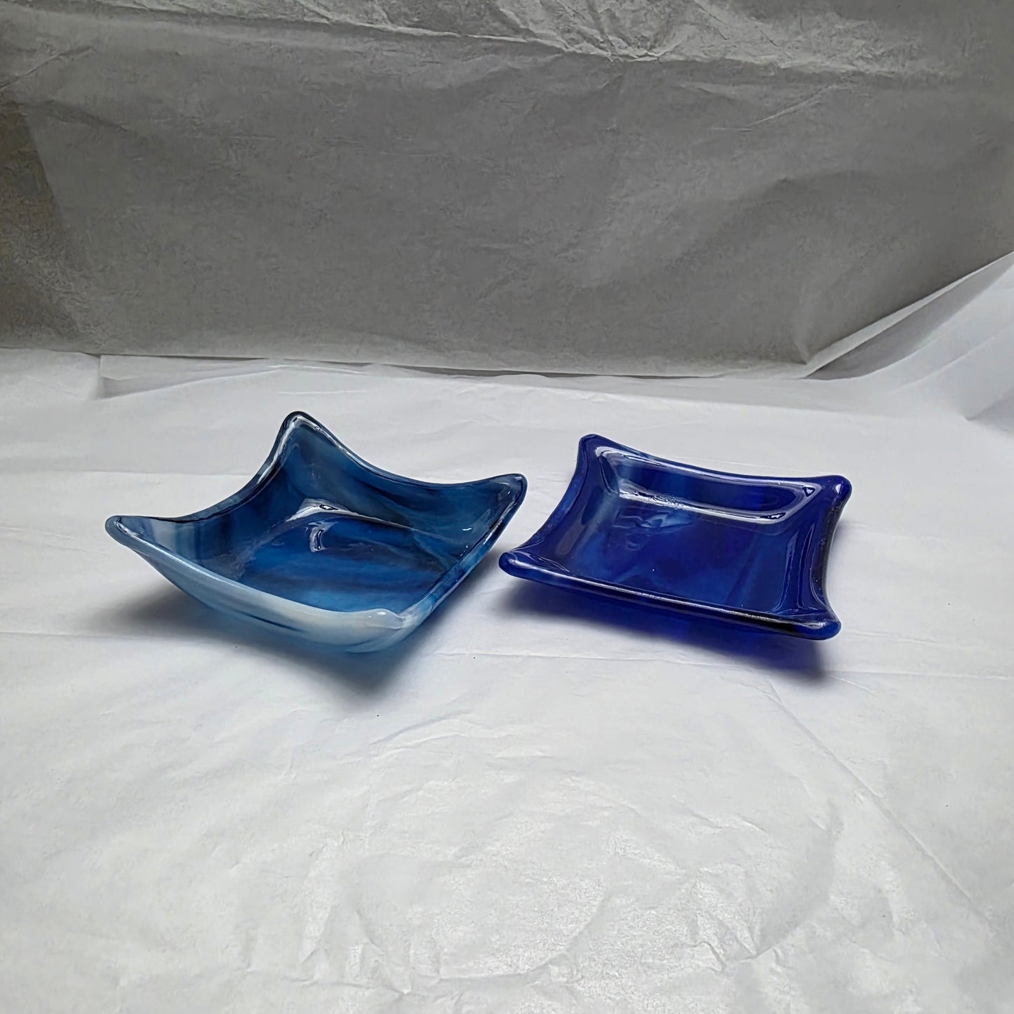 Two little dishes that are streaky white and blue. Dishes are sitting on a white surface.