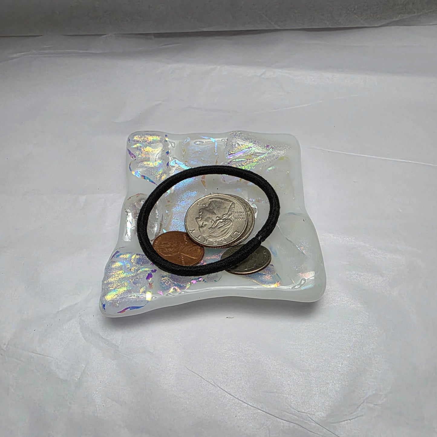 Iridescent ring holder with coins on a white background