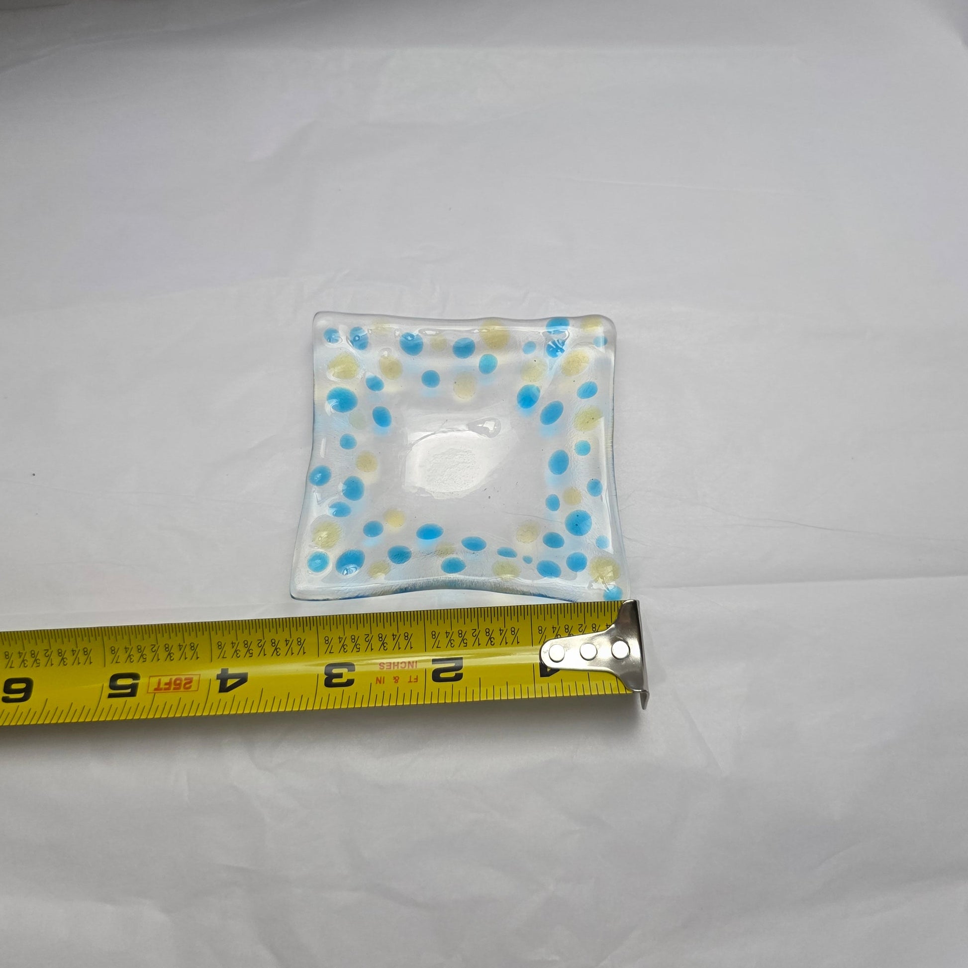 Small square patch with colorful design on a white fabric background, next to a measuring tape for scale.