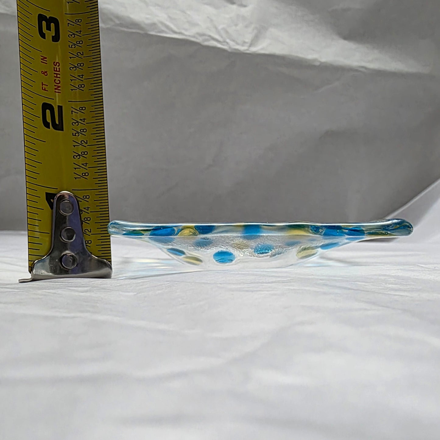 Glass dish with blue and yellow polka dots being measured against a white background
