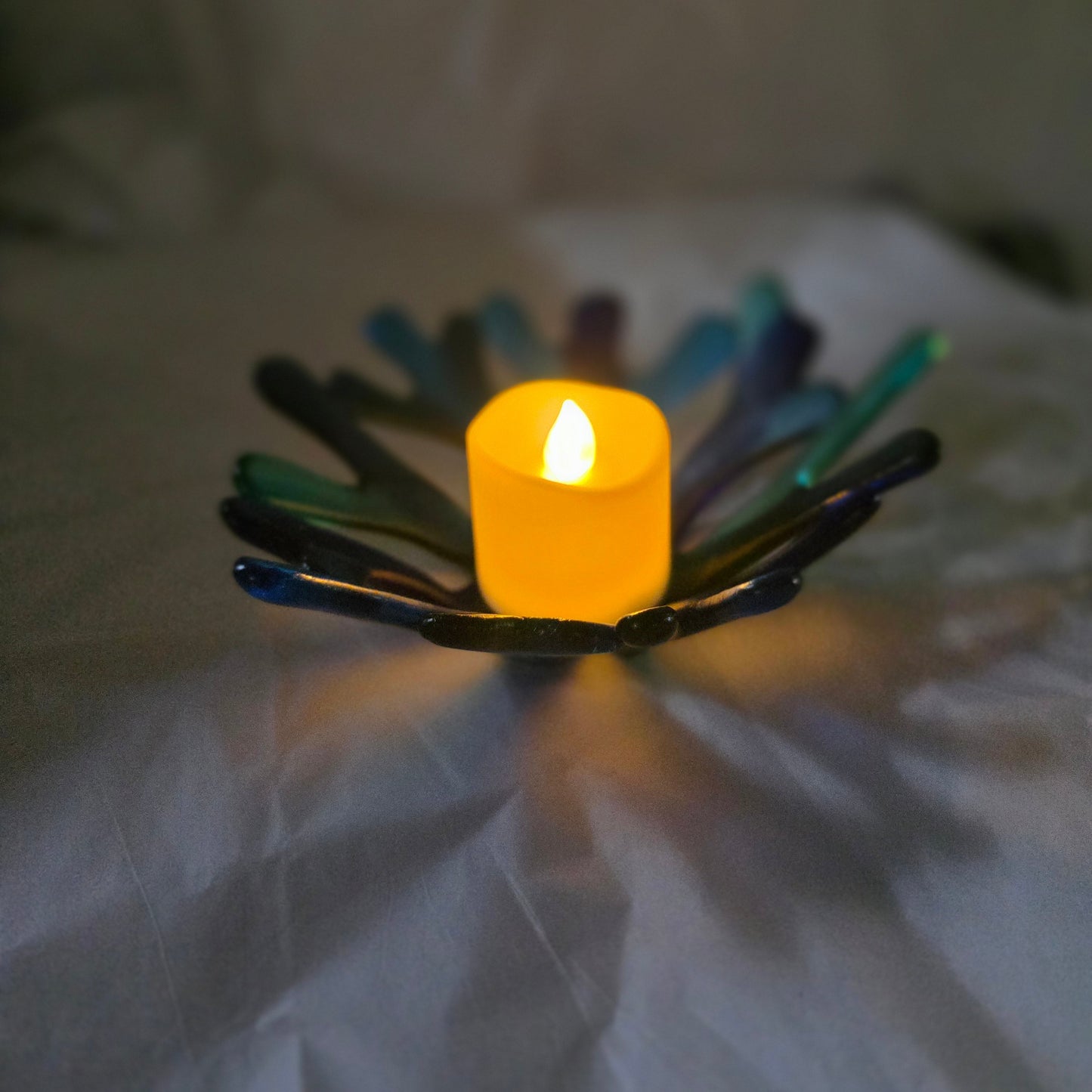 Coral style bowl in varied shades of blue on a white surface, holding a candle, indicating use as a candle holder.  