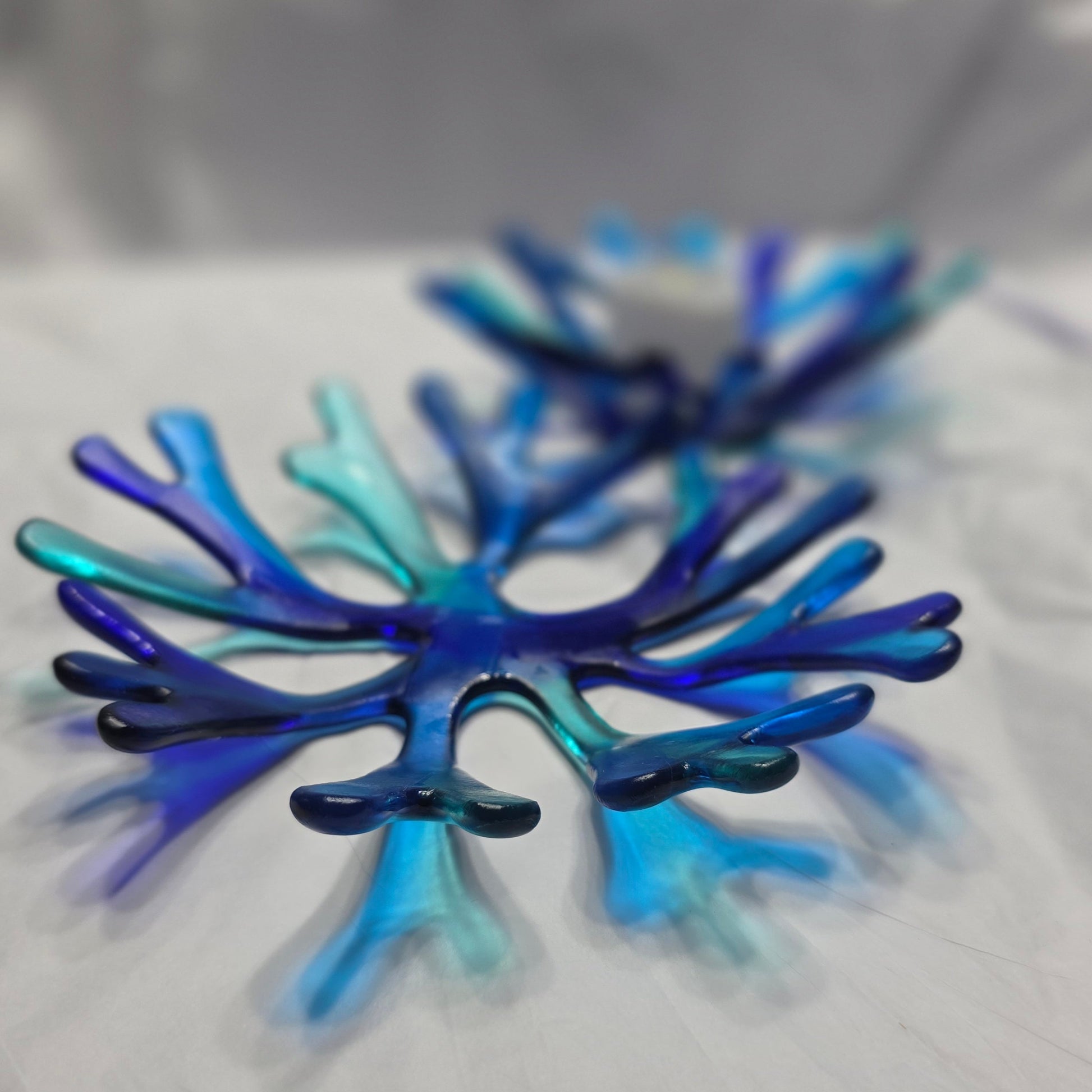 A various shade of blue glass bowl in a coral reef design. The blue coral bowl is sitting on a white surface.