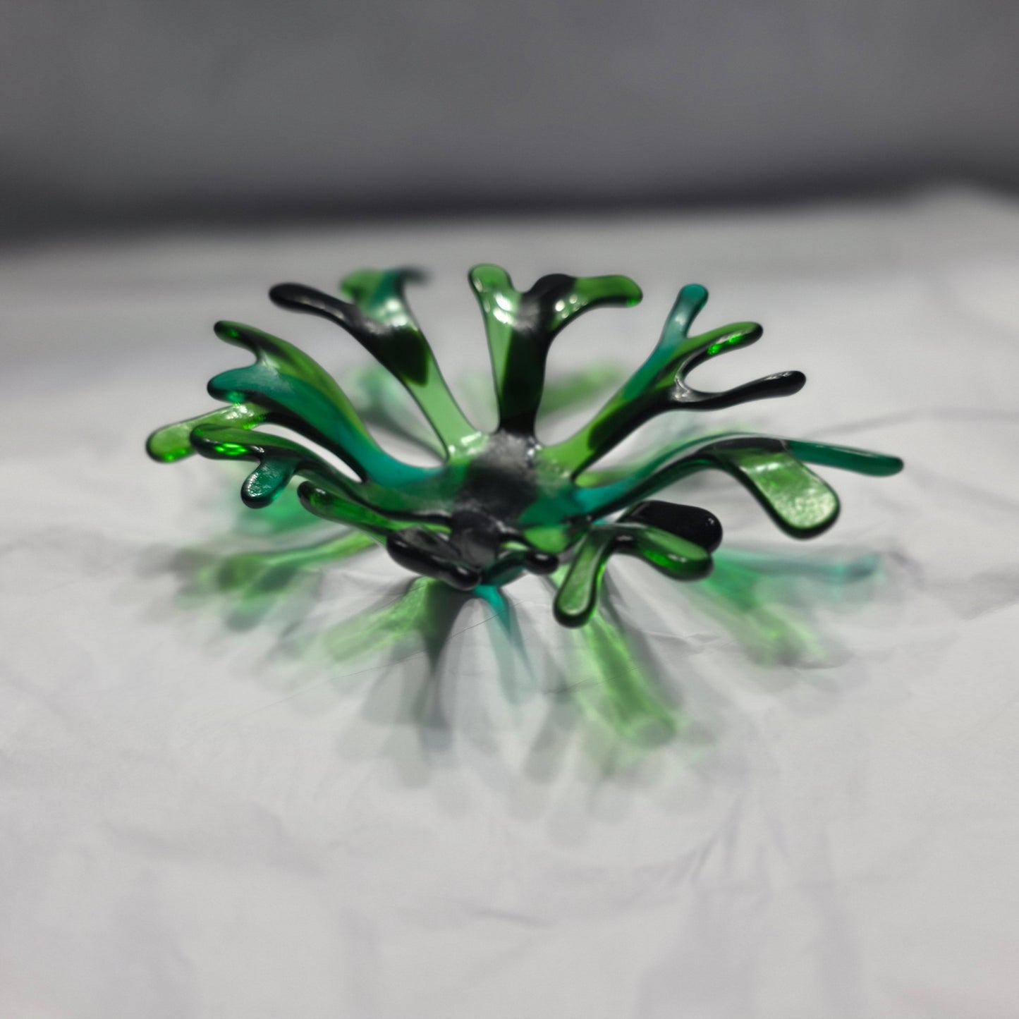 A coral inspired bowl in shades of green, sitting on a white surface.
