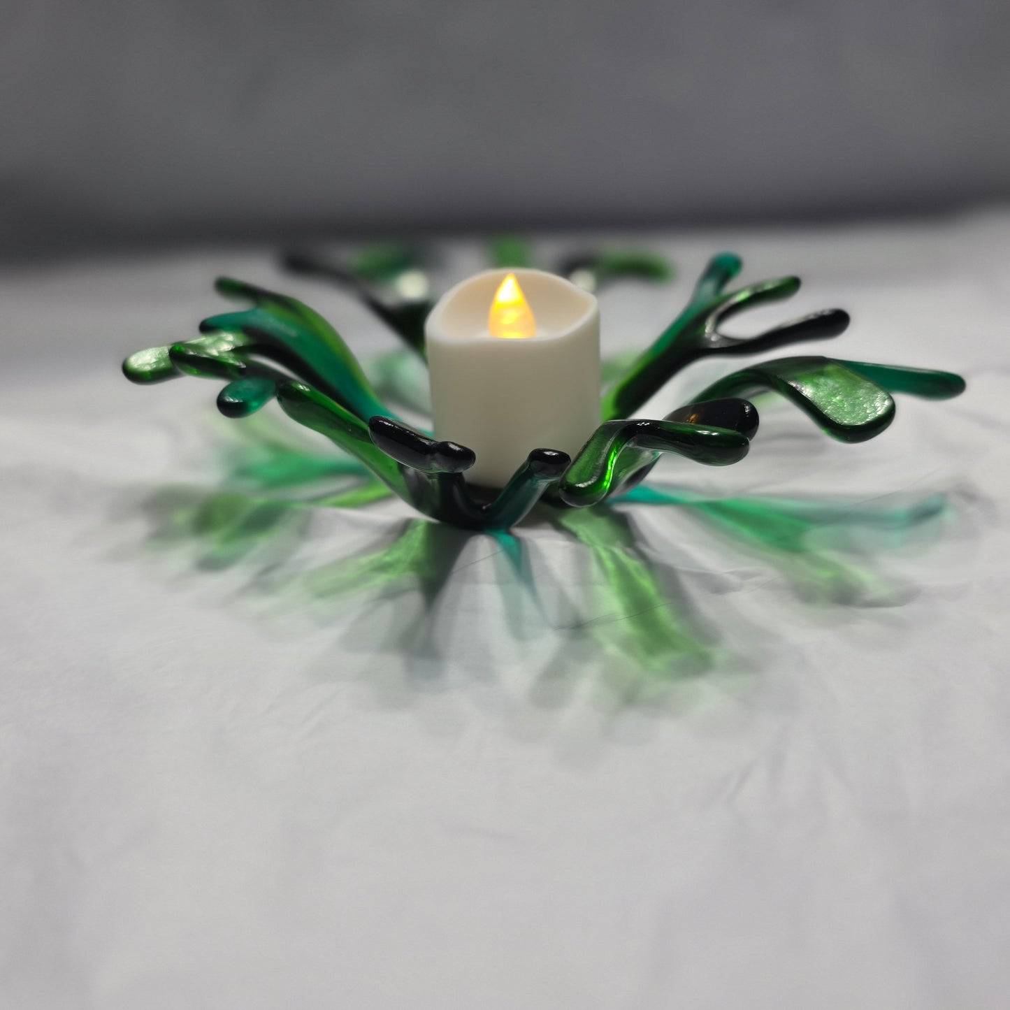 A coral inspired bowl in shades of green, sitting on a white surface. The coral bowl has a candle in it, indicating use as a candle holder.