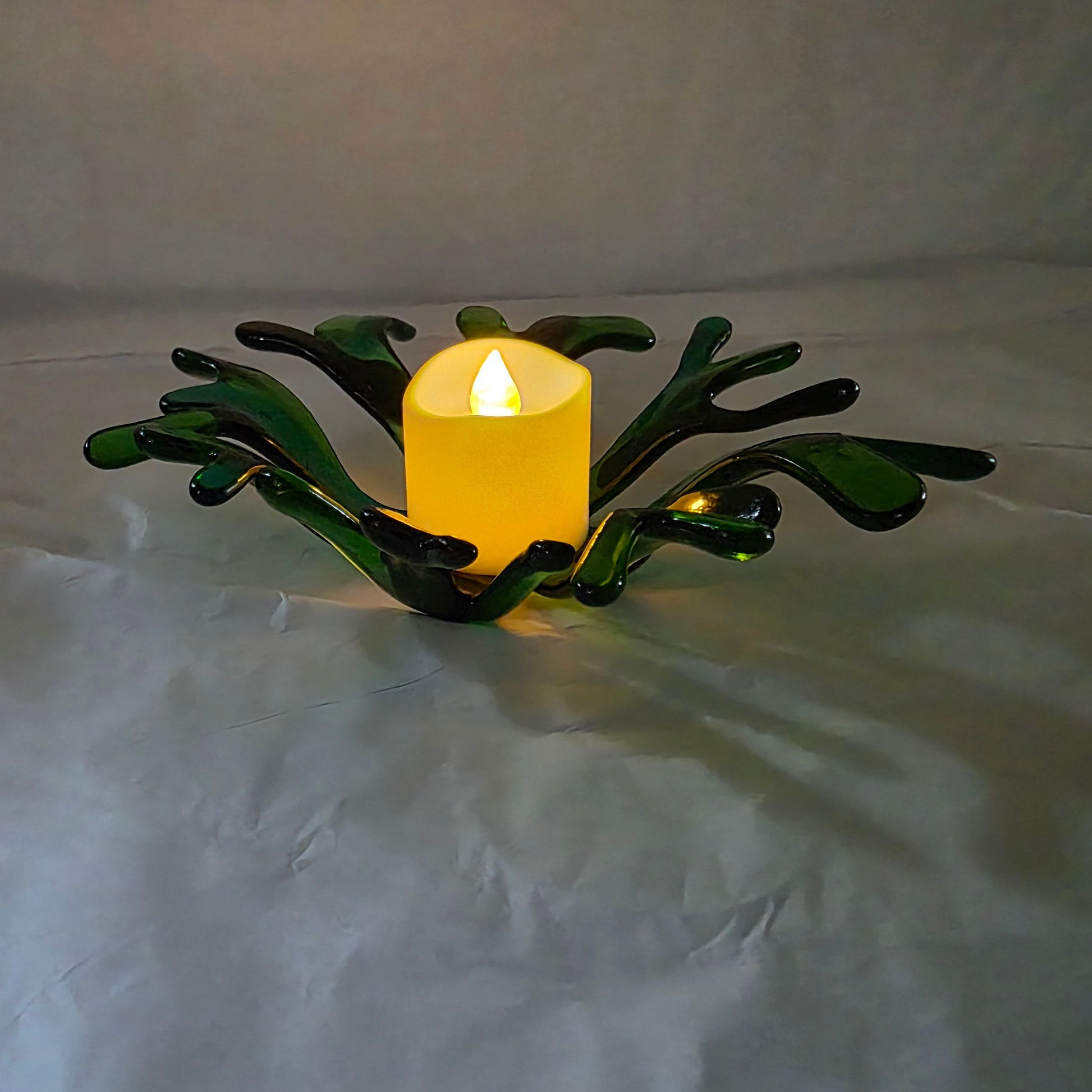 A coral inspired bowl in shades of green, sitting on a white surface. The coral bowl has a candle in it, indicating use as a candle holder.