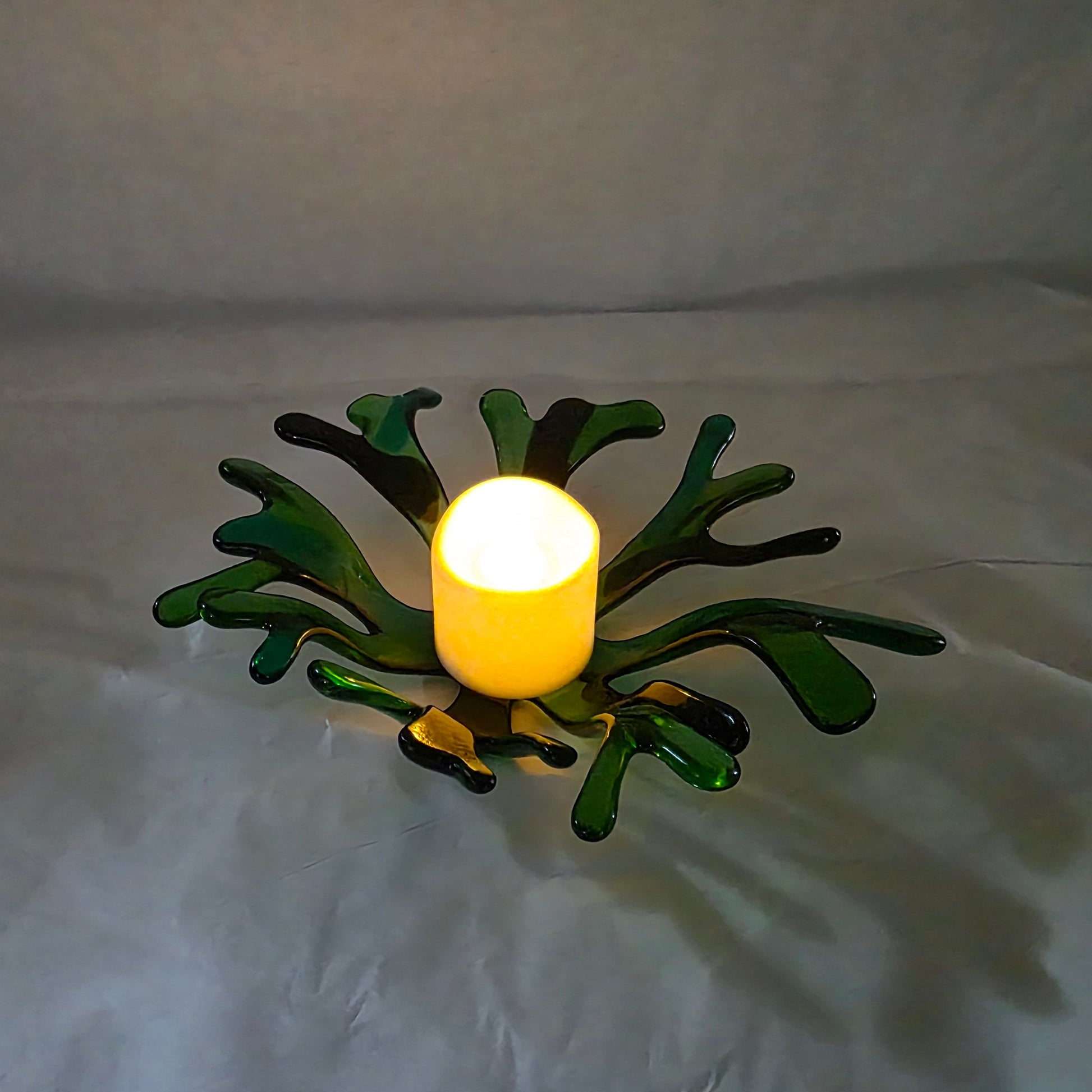 A coral inspired bowl in shades of green, sitting on a white surface. The coral bowl has a candle in it, indicating use as a candle holder.