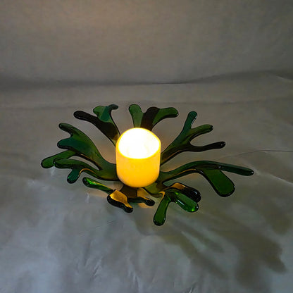 A coral inspired bowl in shades of green, sitting on a white surface. The coral bowl has a candle in it, indicating use as a candle holder.