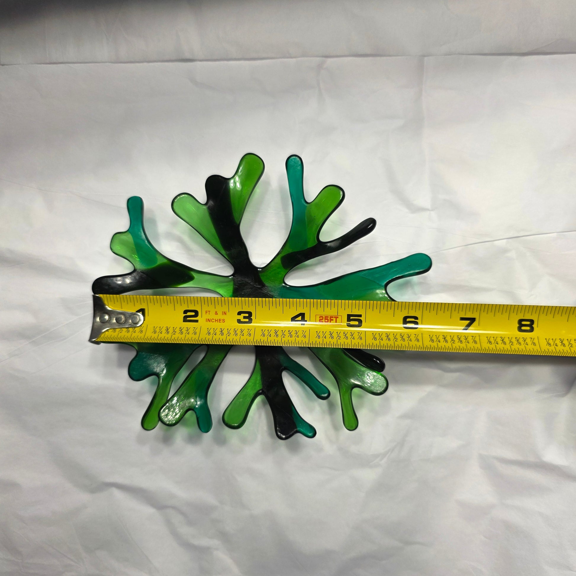 A coral inspired bowl in shades of green, sitting on a white surface. The coral bowl is being shown with a tape measure to indicate approximate size.