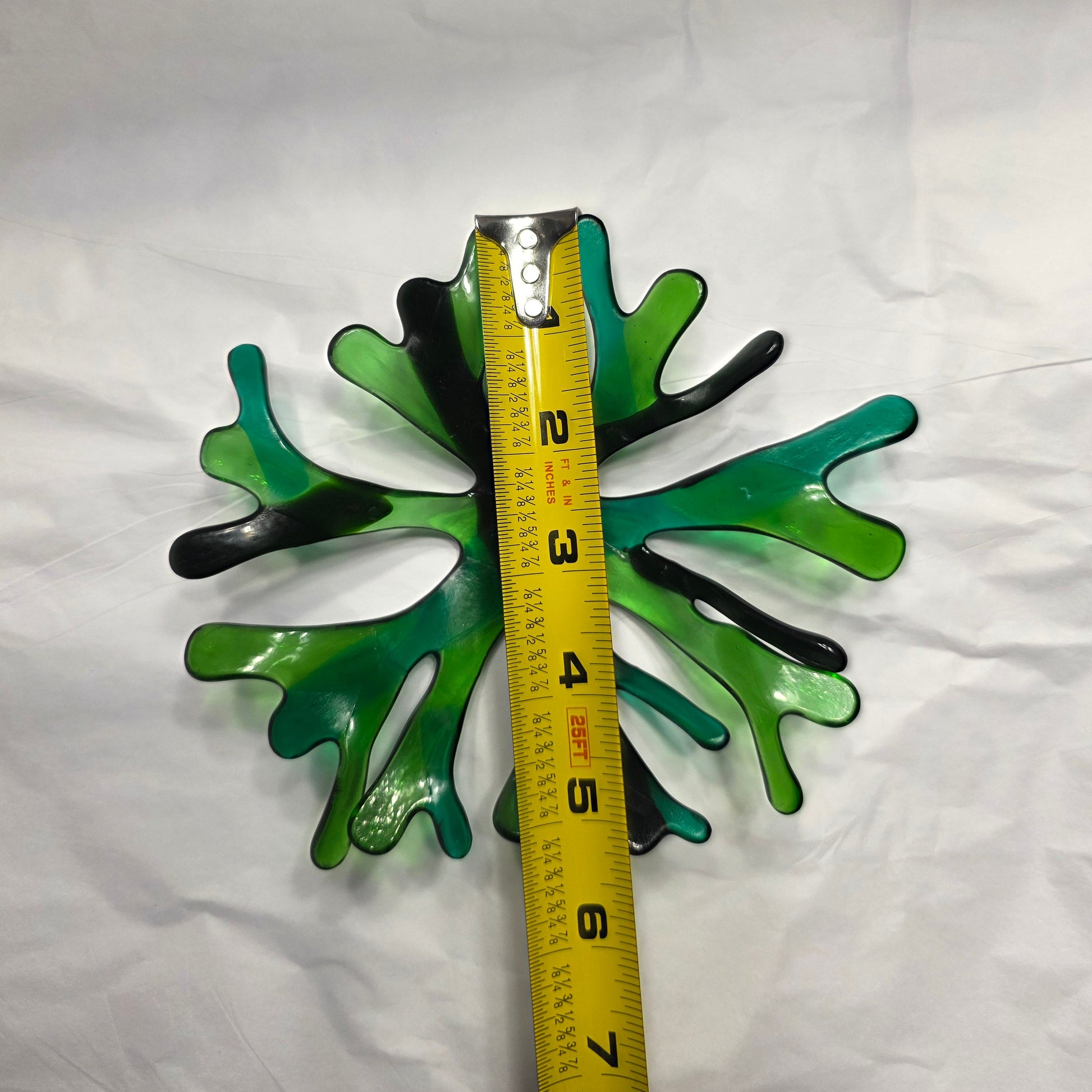 A coral inspired bowl in shades of green, sitting on a white surface. The coral bowl is being shown with a tape measure to indicate approximate size.